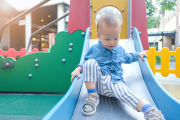 Cute little Asian 18 months / 1 year old toddler baby boy child playing on a slide in playground on summer sunny day, Baby Sliding Down Slide, Kid first experience concept