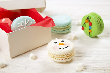 Traditional christmas themed french macaroons sweets in the form of snowman, snowflake, christmas tree and santa's belly with candy cane and white marshmallows on the white wooden table.  Close up.