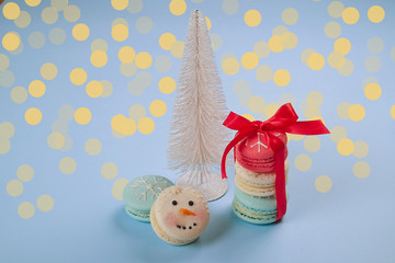 Traditional french macaroons sweet treats, christmas themed, shaped as santa's belly, snowflake, snowman, pine tree on blue bsckground, bokeh, close up.