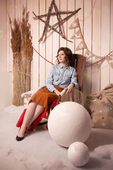 Brunette sitting on a old chair in a denim shirt and brown skirt in vintage interiors with a star made from twigs on the wall