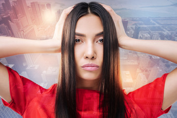 Fototapeta premium New haircut. Gorgeous young attentive woman looking serious while standing with her hands touching the head and evaluating the quality of her new haircut