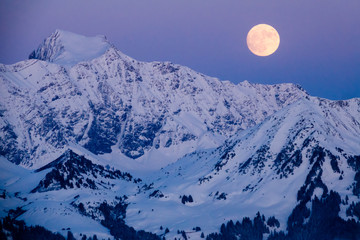 full moon rising in the evening sky in the Swiss Alps over a winter mountain landscape near Klosters
