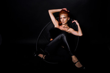 Fototapeta na wymiar Fashion model red haired girl with originally make up like leopard predator isolated on black. Studio portrait on chair.