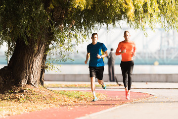 Handsome young men wearing sportswear and running at quay during autumn