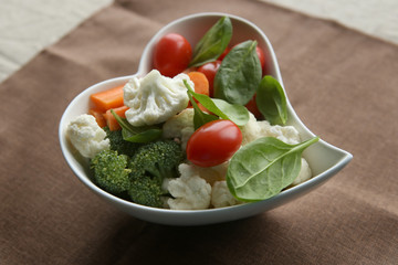 Heart shaped plate with fresh vegetables. Raw vegetables (tomatoes, cauliflowers, broccoli, carrots, spinach) ingredients for snack, salad or soup.