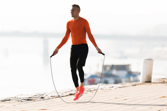 Handsome young man wearing sportswear and  skipping rope at quay during autumn