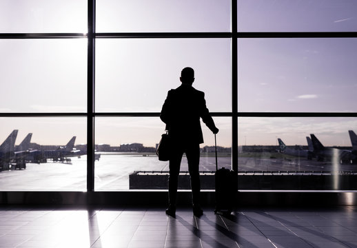 Man standing in airport, silhouette against glass wall