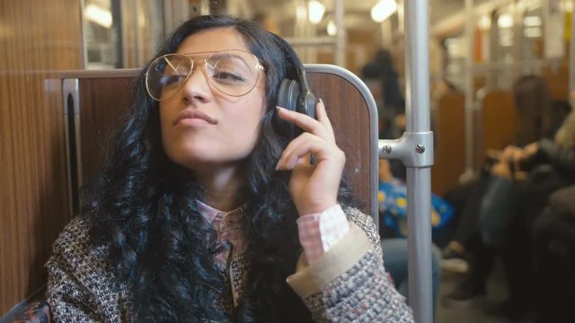 portrait of stylish and fashionable brunette rides in a train car and listens with music on headphones with pleasure Video slowed to 2 times the actual speed
