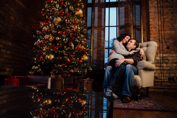  Beautiful couple kissing in armchair near christmas tree at new year eve