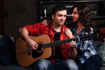 couple is sitting on the couch with a guitar. Long hair of a brunette with an acoustic guitar.