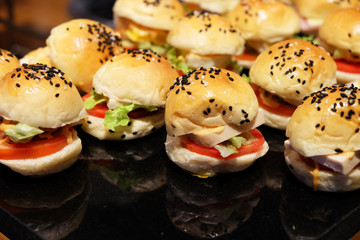 Many little size of ham cheese burgers on the black shiny plate