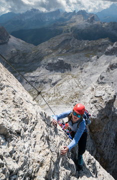 attractive young female climber on a steep Via Ferrata in the Italian Dolomites with a great view