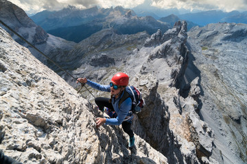 attractive young female climber on a steep Via Ferrata in the Italian Dolomites with a great view