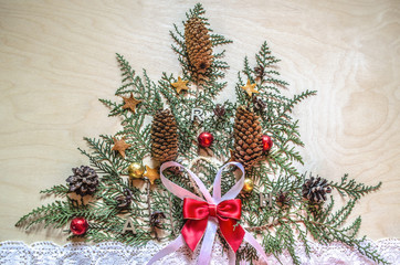 Light plywood with a Christmas tree, made of twigs thuja with fir cones and chocolate balls on a lace ribbon
