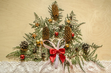 Christmas tree, made from twigs of thuya with fir cones and chocolate balls and lace ribbon on wooden plywood