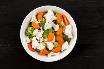 Fresh salad with raw broccoli, cauliflower and carrot in a white dish, top view
