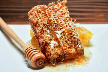 Fresh honeycombs and wooden dipper with pouring honey on a wooden table
