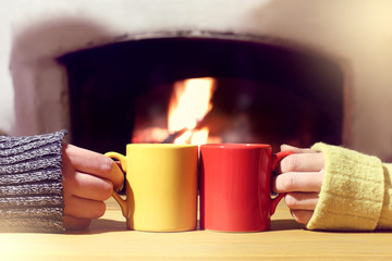 cozy evening for winter vacations together/ red and yellow mug in the hands of a couple of people basking at the fireplace