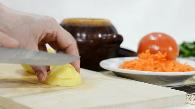 Slicing potatoes for hot dishes roast in a clay pot closeup