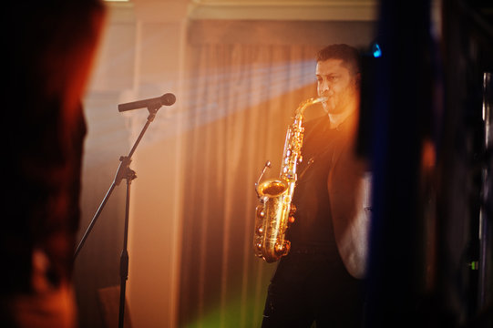 Musicial music live band performing on a stage with different lights. Saxophonist plays.