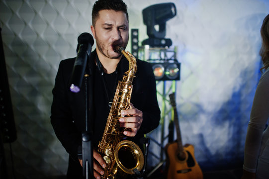 Musicial music live band performing on a stage with different lights. Saxophonist plays.