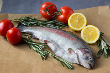 Two raw fish. Fresh trout with lemons, tomatoes and greens.