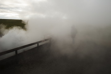 Fototapeta na wymiar Geothermal plant steam/Unrecognizable person walking trough the steam produced by the hot sulphureous water geysers where a geothermal plant is thus enabling the heating system.