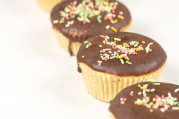Vanilla cupcakes with chocolate cream and colorful sprinkles isolated on white background
