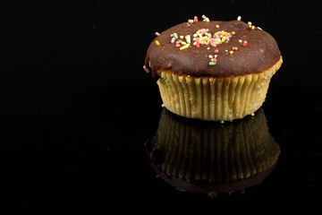 Vanilla cupcakes with chocolate cream and colorful sprinkles above black reflections background