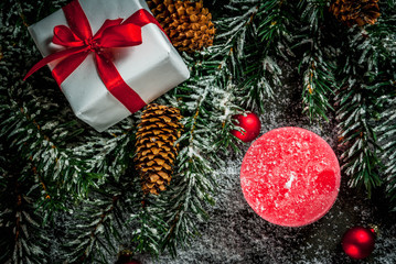 Christmas background for greeting card. Christmas tree branches with snow effect with festive red ribbon, pine cones, gift boxes and candles, on dark blue background, copy space top view