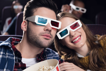 young couple in 3d glasses with popcorn watching movie in cinema