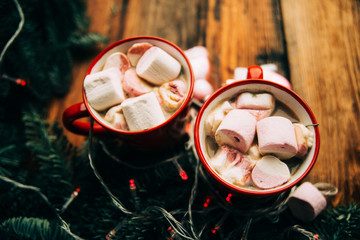 Two cups of hot chocolate with marshmallows and candy canes and red christmas malls on a dark wooden background. Place for text