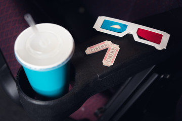 tickets, 3d glasses and paper cup with soda on seat in movie theater