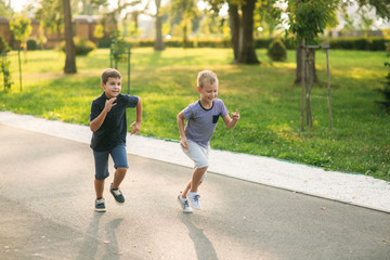 Obraz premium Two children are playing in the park. Two beautiful boys in T-shirts and shorts have fun smiling. They eat ice cream, jump, run. Summer is sunny
