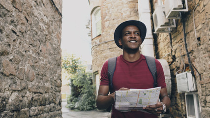 African american tourist man walking and watching paper city map to find directions to famous place