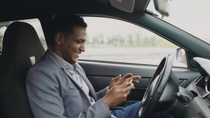 Happy african american businessman surfing social media on his tablet computer sitting inside his car