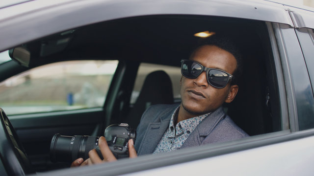 Private detective man sitting inside car and photographing with dslr camera