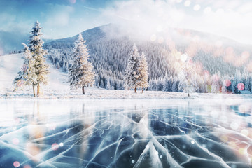 Blue ice and cracks on the surface of the ice. Frozen lake in winter mountains. It is snowing. The hills of pines. Winter. Carpathian Ukraine Europe