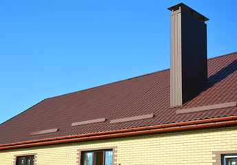 New installed brown metal tiled roof with plastic rain gutter system, snow board protection, chimney, house roofing construction outdoor.