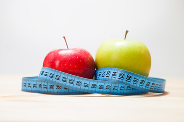 The concept of weight loss, healthy eating. Two apples, red and green, a measuring tape on the table.