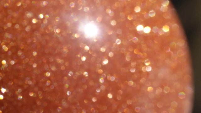 MACRO DOF: Beautiful decorative orange sunstone sparkling in bright sunlight. Sunstone semi precious stone glittering in bright sunshine. Reflective golden round stone emitting strong rays of light.