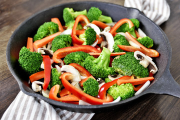 Fresh vegetables in an iron pan. Healthy eating or scene with fresh broccoli, onion, mushrooms, carrots and red bell pepper. Cooking pan on a wooden table.