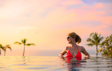Obraz na płótnie Canvas Woman enjoying sunset while relaxing in infinity pool
