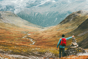 Man placing stone to rock cairn marking route hiking in mountains with backpack Travel healthy...