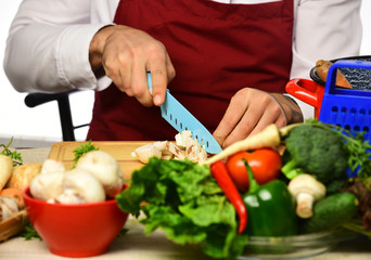 Cook burgundy uniform cuts vegetables. Male hands cut mushroom