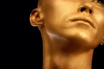 The guy painted in gold paint. completely. portrait. beauty on a black background. Shiny mouth nose and neck, and ear are golden. He looks up. for design with space for text.