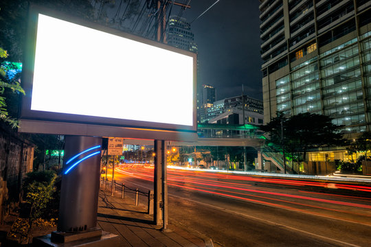 Blank Template For Outdoor Advertising Or Blank Billboard With Light Trail To Business District In Twilight.