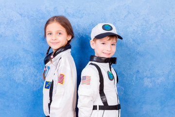 Young children boy and girl playing in astronaut in white astronaut costume and dreaming about flying into cosmos on blue background © Monstar Studio