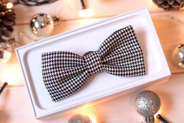 Bow tie and white gift box on New Year wooden table, top view. Gift to man for new year, men's accessories.