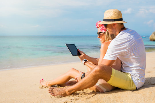 Couple using tablet on the beach
